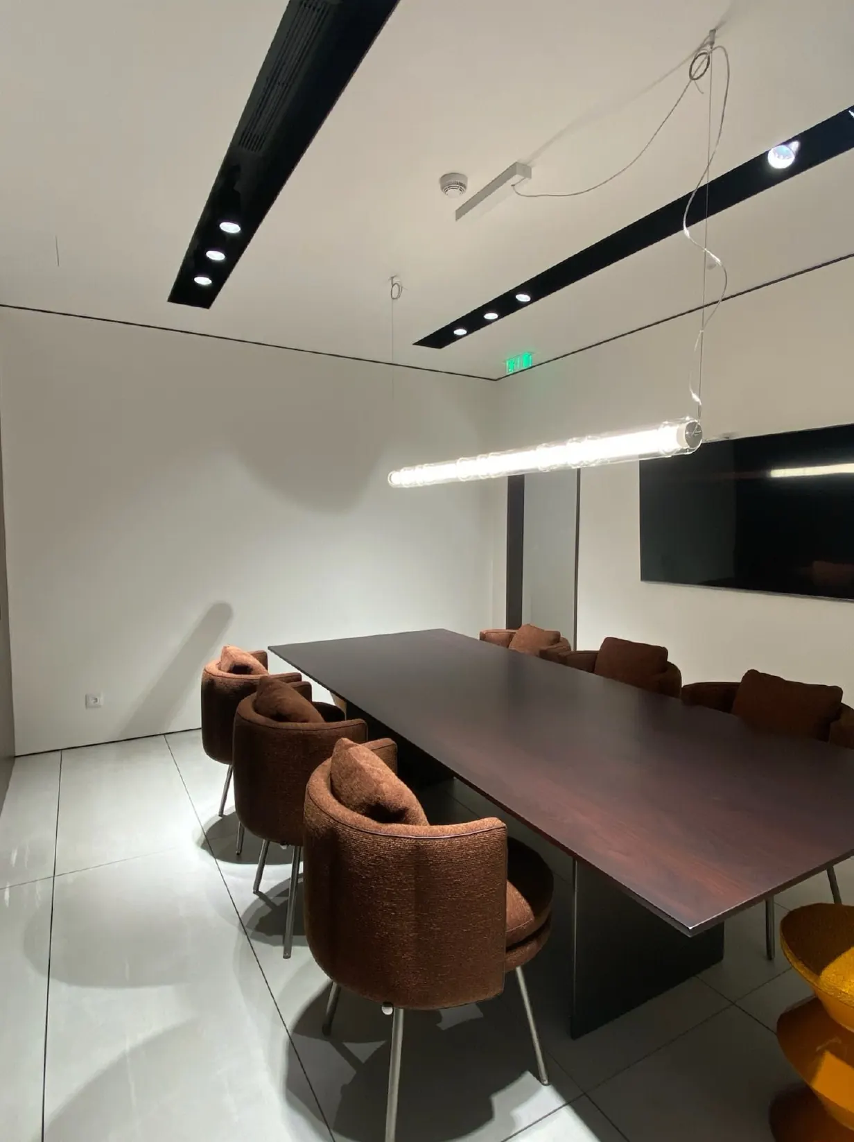 Sala de reuniões com mesa escura, cadeiras em veludo castanho e paredes em marmorino claro