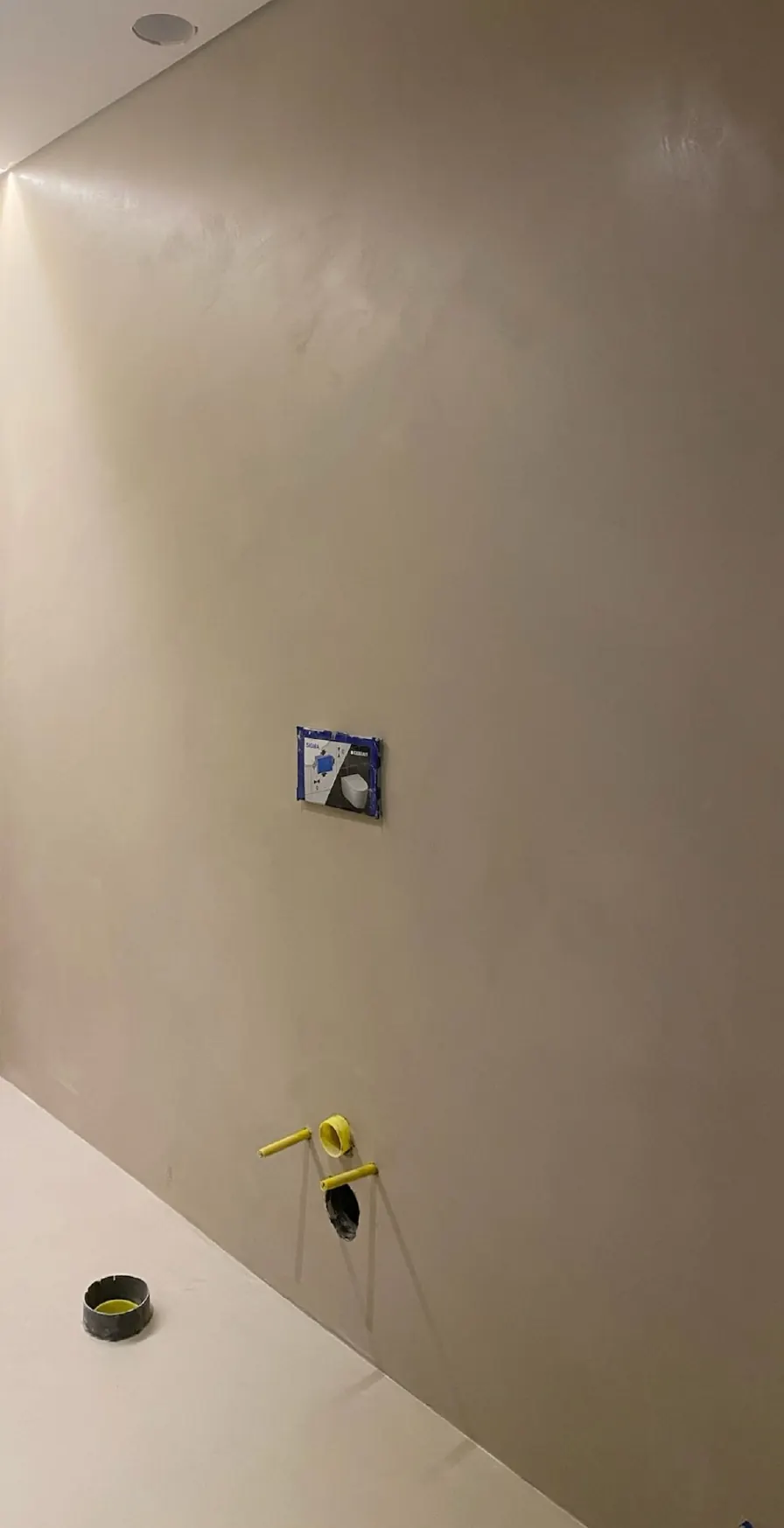Parede em microcimento cinza durante a aplicação, com caixa de interruptor à vista