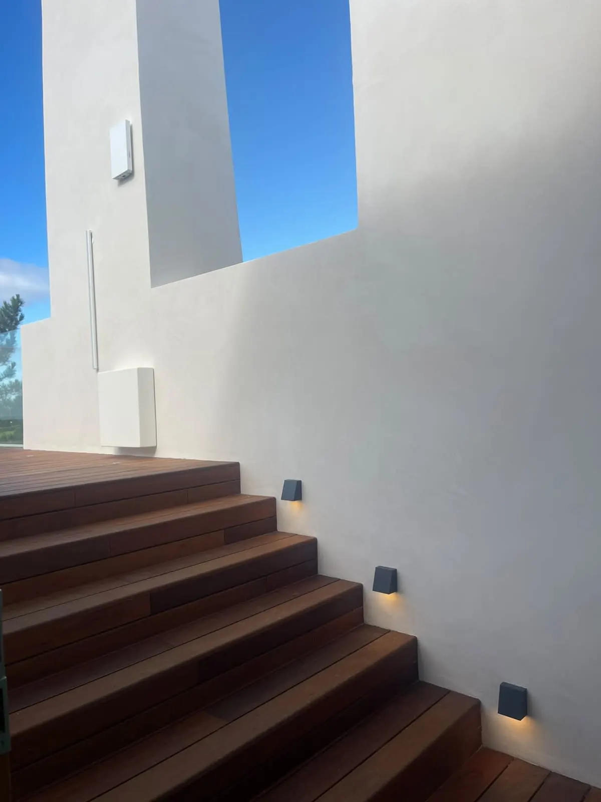 Escada exterior de madeira junto a parede branca contínua da moradia